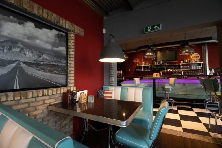 Amerikaans diner interieur met rode muren, turkoois-witte zithoek, zwart-wit landschapsfoto en bar met paarse verlichting.