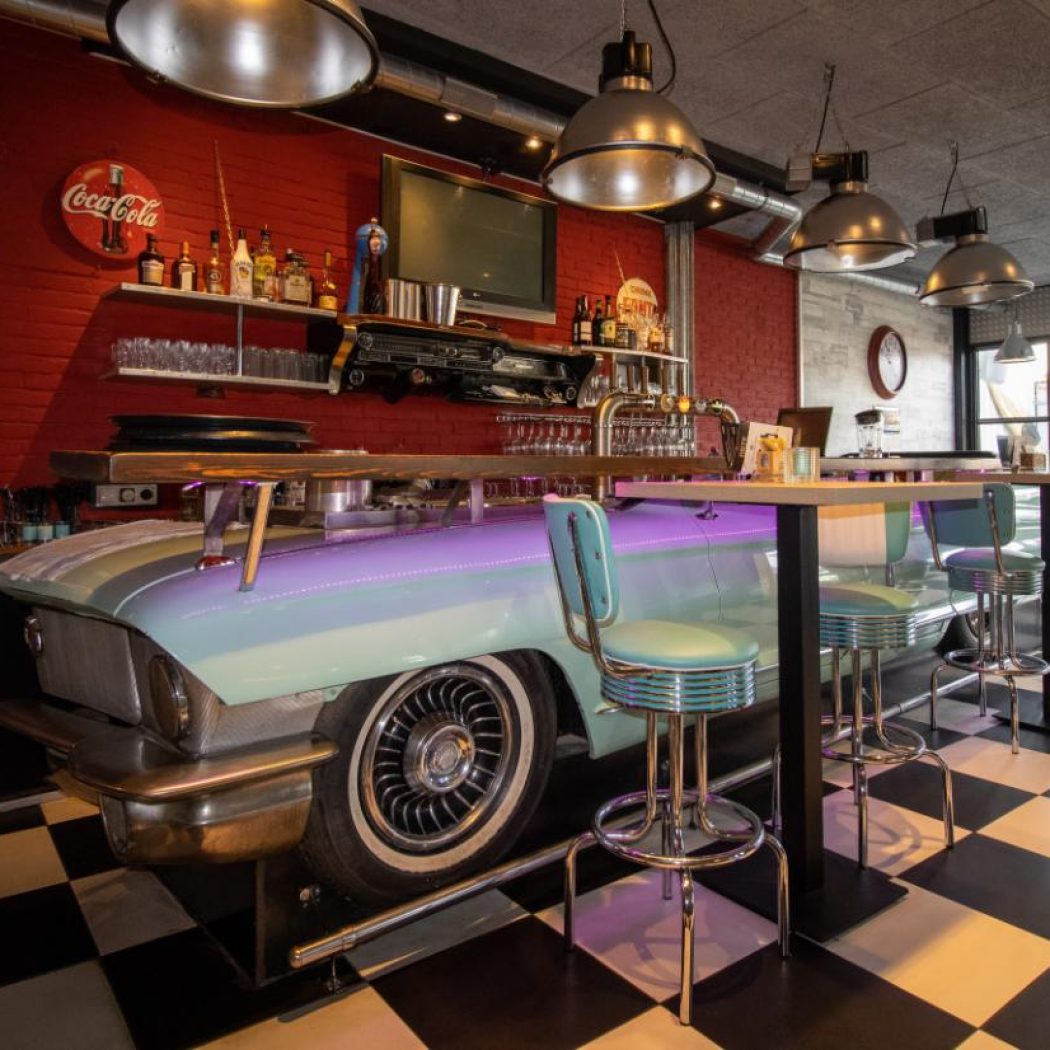 Retro bar interieur met lichtblauwe auto als bar, bijpassende barkrukken, rode bakstenen muur en Coca-Cola bord.