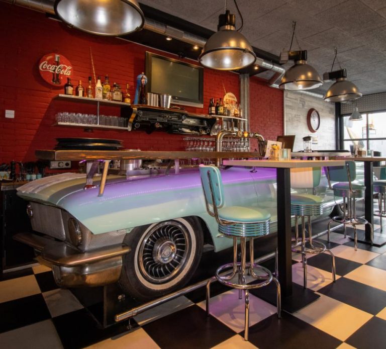 Retro bar interieur met lichtblauwe auto als bar, bijpassende barkrukken, rode bakstenen muur en Coca-Cola bord.