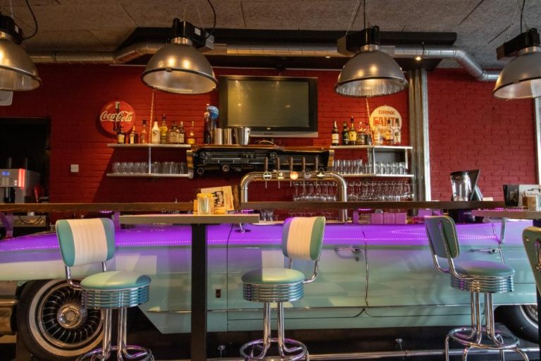 Bar in Amerikaanse retrostijl met een lichtblauwe oldtimer als bar, paarse verlichting en chromen krukken.