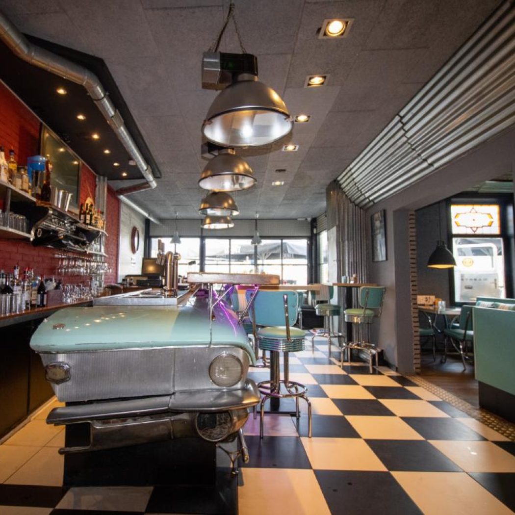 Retro dinerbar met lichtblauwe oldtimer toonbank, Coca-Cola reclamebord en zwart-wit geblokte vloer.