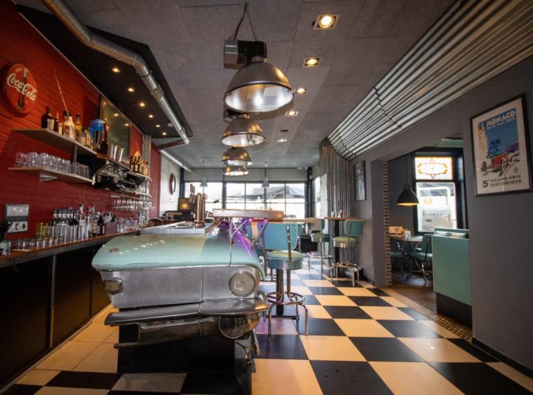 Retro dinerbar met lichtblauwe oldtimer toonbank, Coca-Cola reclamebord en zwart-wit geblokte vloer.