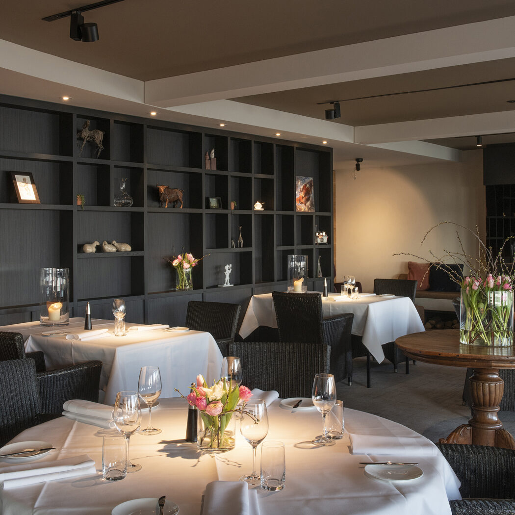Sfeervol restaurantinterieur met gedekte tafels, donkere kastenwand en verse bloemstukken.