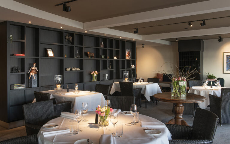 Sfeervol restaurantinterieur met gedekte tafels, donkere kastenwand en verse bloemstukken.