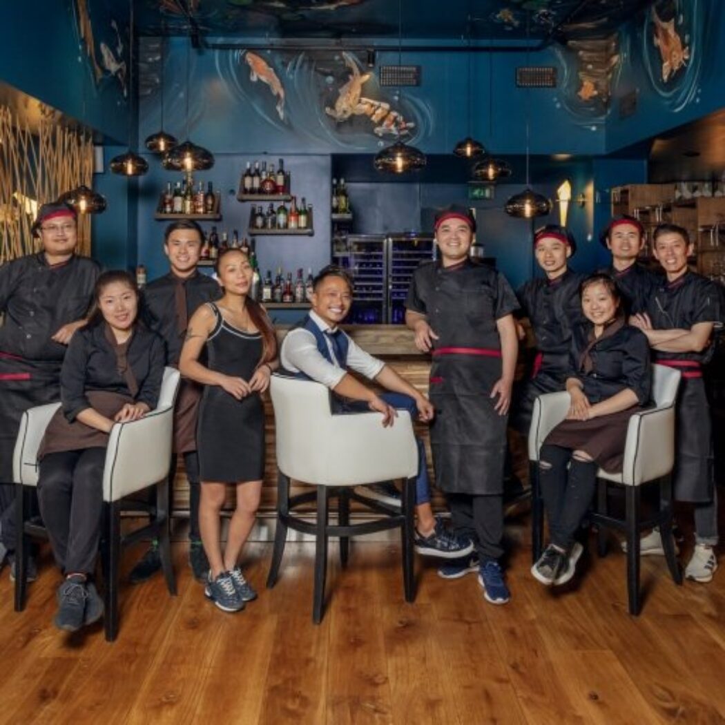 Lachend restaurantteam van chefs en medewerkers poseren voor een bar in een modern restaurant met koivissen op de muur.