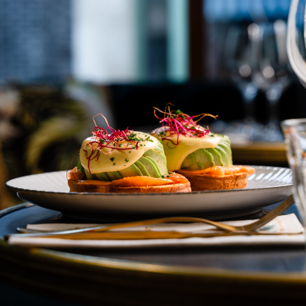 Twee eggs benedict met avocado, gerookte zalm en rode spruiten op een bord.