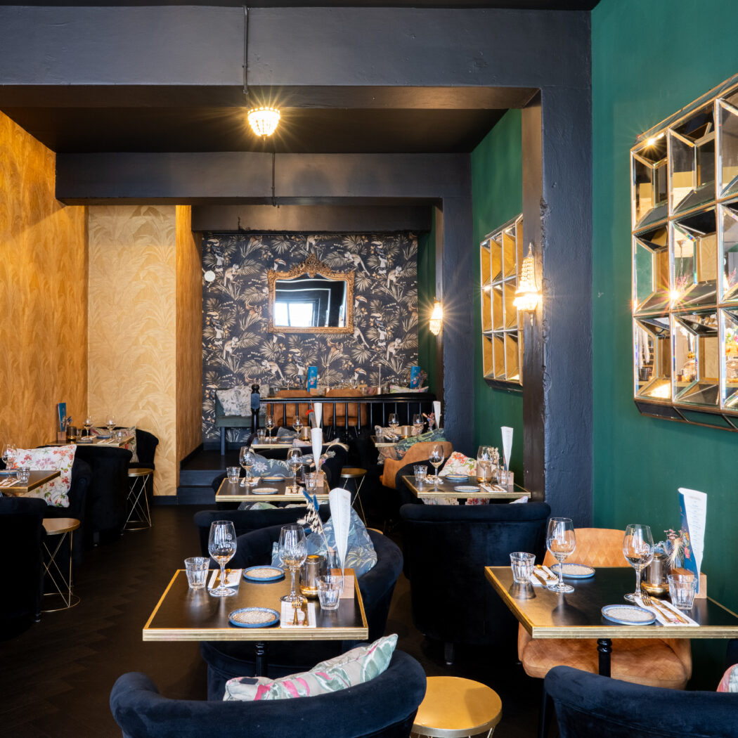 Stijlvol restaurantinterieur met gouden, groen en tropisch behang, spiegels en gedekte tafels.