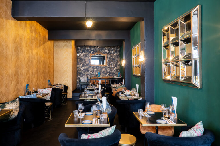 Stijlvol restaurantinterieur met gouden, groen en tropisch behang, spiegels en gedekte tafels.