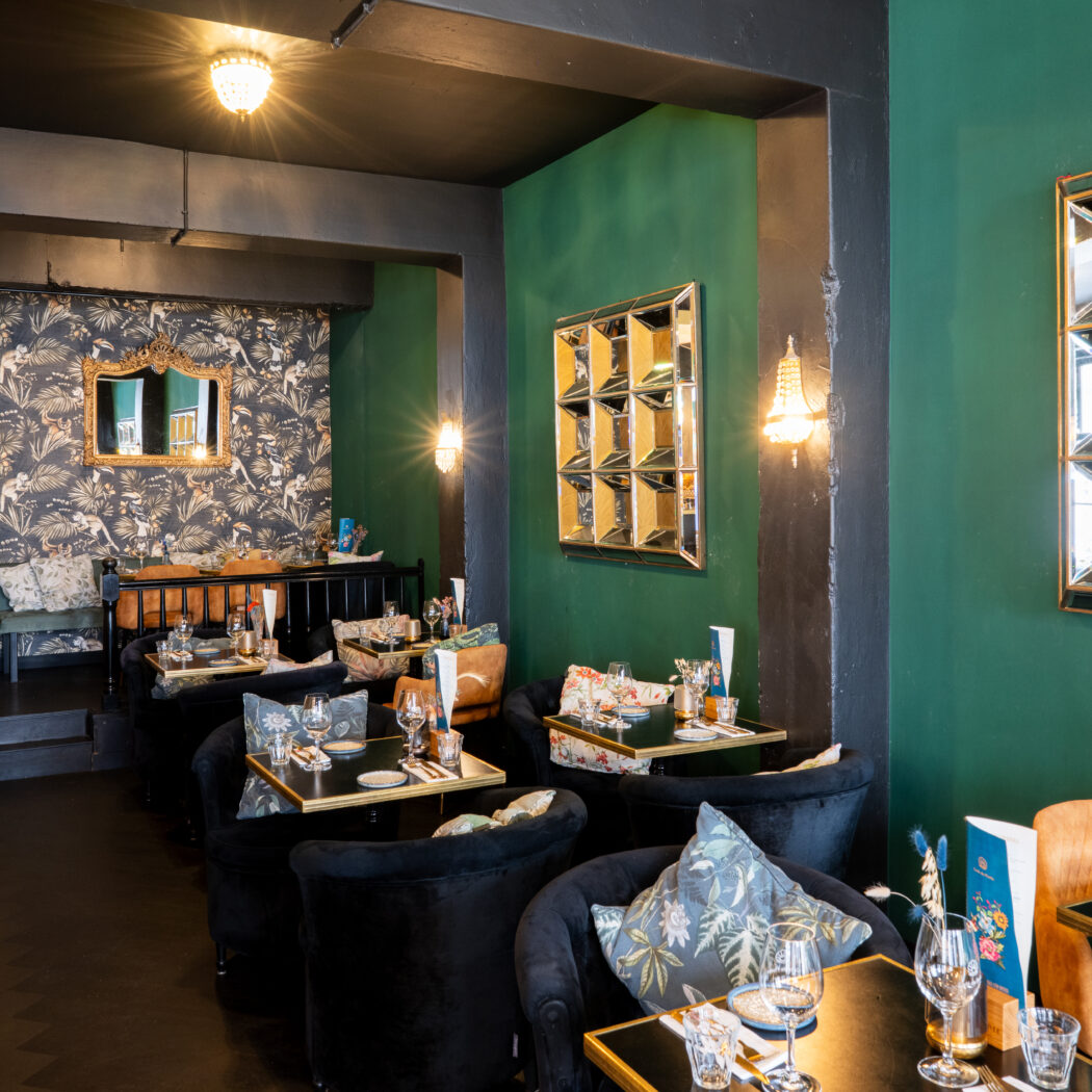 Sfeervol restaurantinterieur met zwarte fluwelen stoelen, gedekte tafels en groene muren.