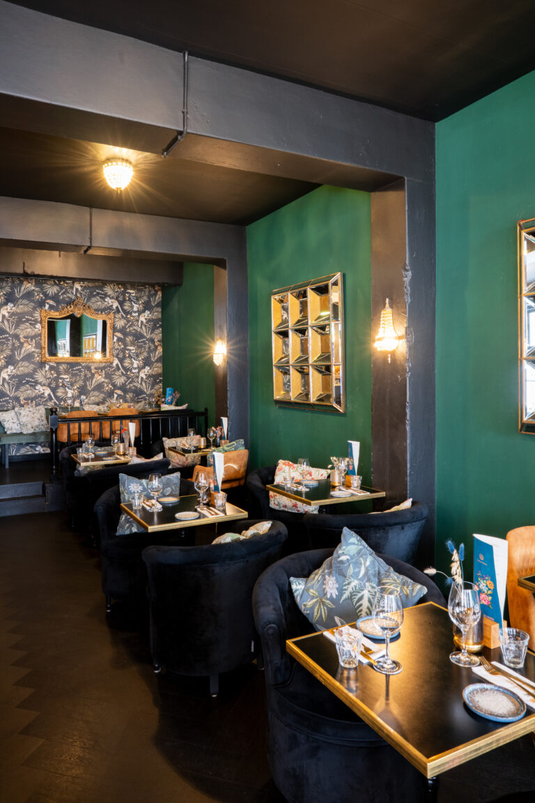 Sfeervol restaurantinterieur met zwarte fluwelen stoelen, gedekte tafels en groene muren.