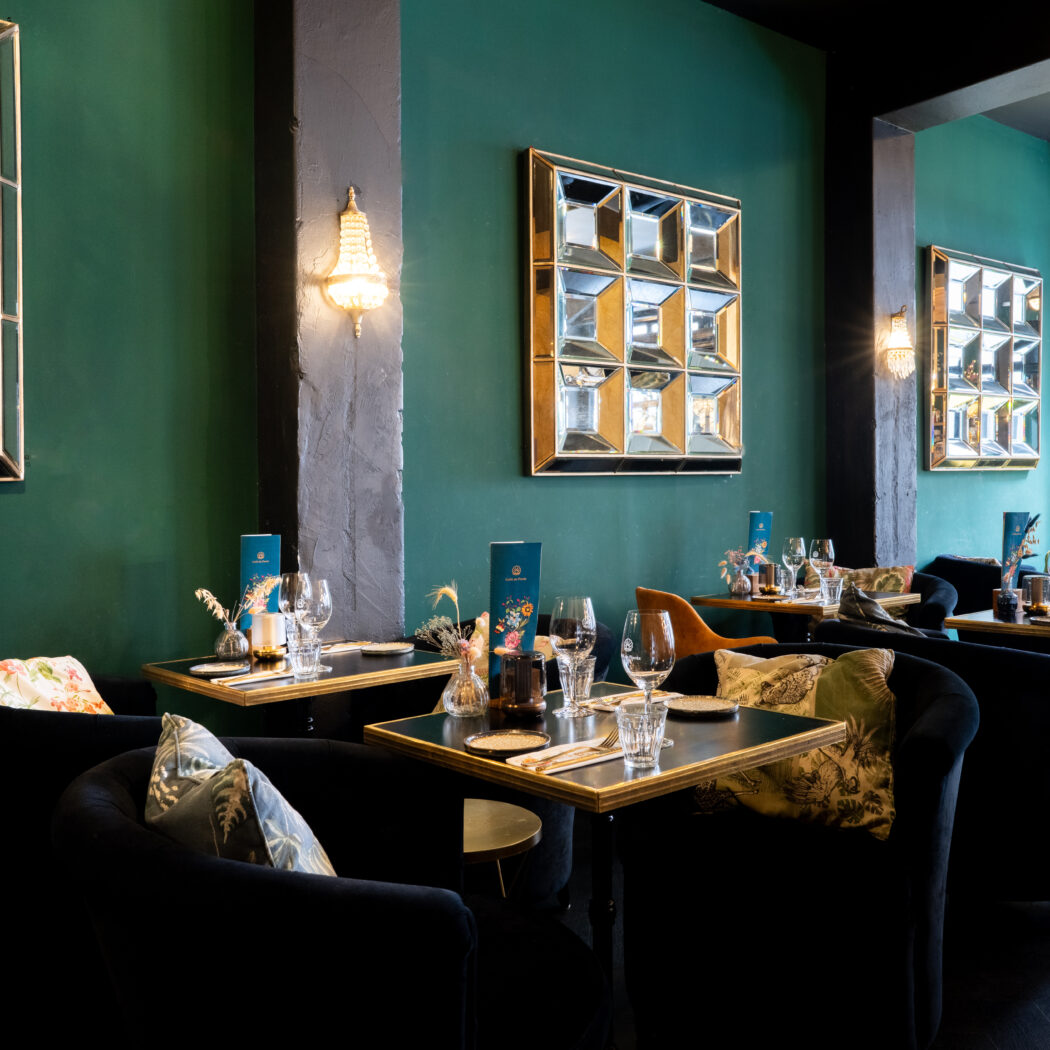 Sfeervol restaurant met diepgroene muren, fluwelen stoelen, gedekte tafels en decoratieve spiegels.