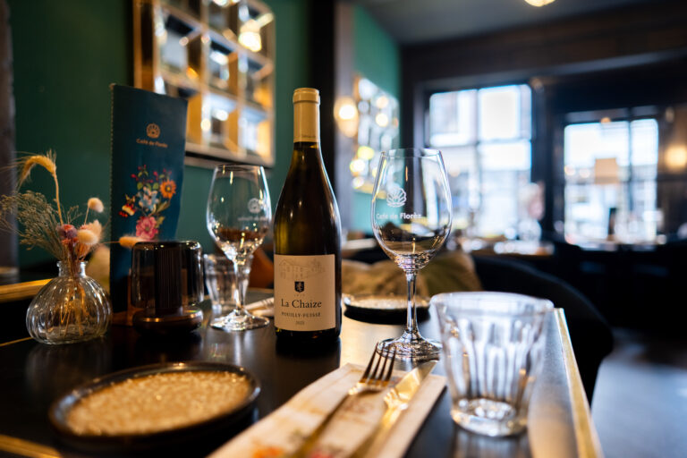 Fles La Chaize Pouilly-Fuissé witte wijn, wijnglazen met Café de Florez logo, menu en gedroogde bloemen op tafel.