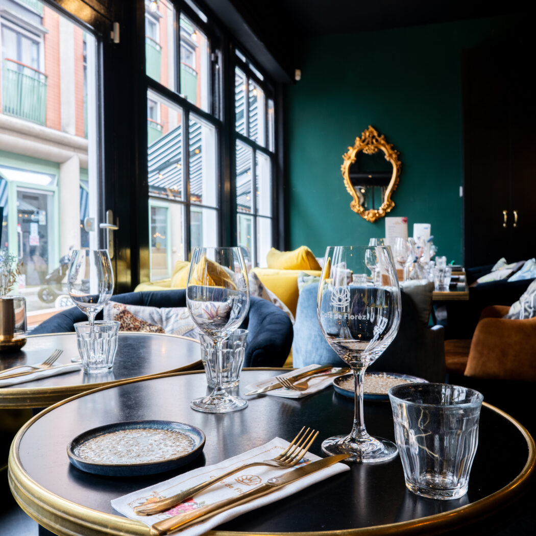 Sfeervol restaurant interieur van Café de Florez met gedekte tafels, glaswerk, gouden bestek en een groen-zwarte muur.
