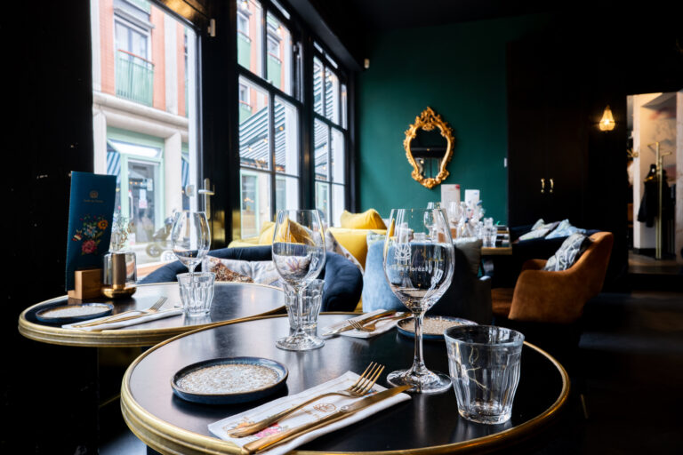 Sfeervol restaurant interieur van Café de Florez met gedekte tafels, glaswerk, gouden bestek en een groen-zwarte muur.