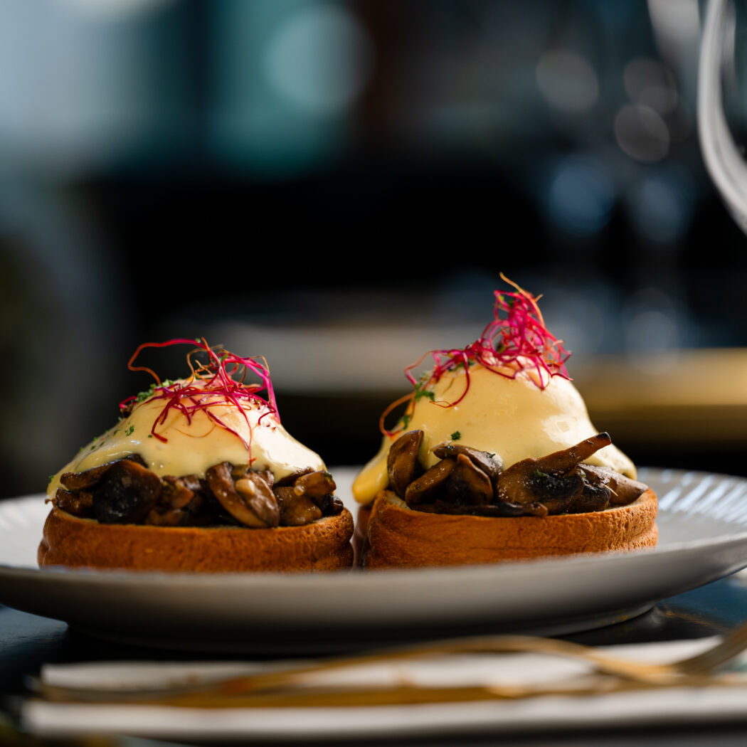 Twee hartige toasts met gebakken paddestoelen, romige saus en rode kiemen op een witte schaal.
