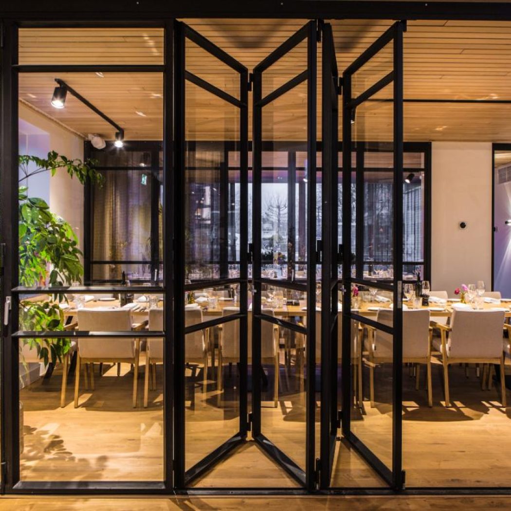 Modern restaurant met open zwarte stalen vouwdeuren en een lange gedekte houten eettafel.