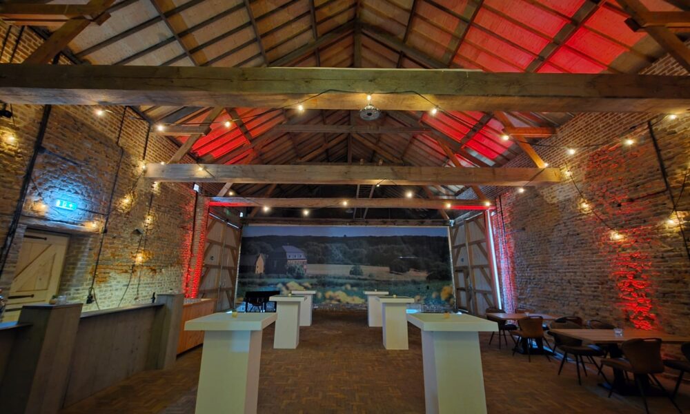 Sfeervolle evenementenlocatie met bakstenen muren, houten balken, rode verlichting en statafels.