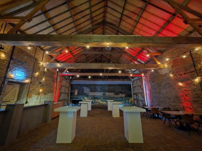 Sfeervolle evenementenlocatie met bakstenen muren, houten balken, rode verlichting en statafels.