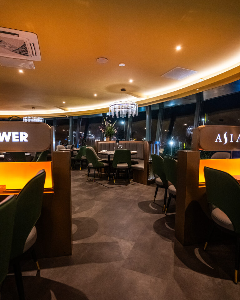 Sfeervol restaurantinterieur s avonds met ronde banken, donkergroene stoelen, kroonluchter en oplichtende WER en ASIA borden.