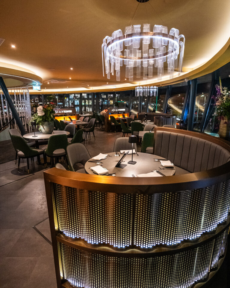 Luxe restaurant Asian Tower met ronde zitbanken, een glazen kroonluchter en uitzicht op de verlichte stad s nachts.