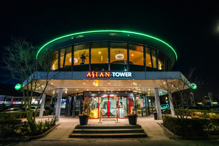 Het ronde restaurant Asian Tower s nachts, met opvallende groene neonverlichting en een warm verlicht interieur.