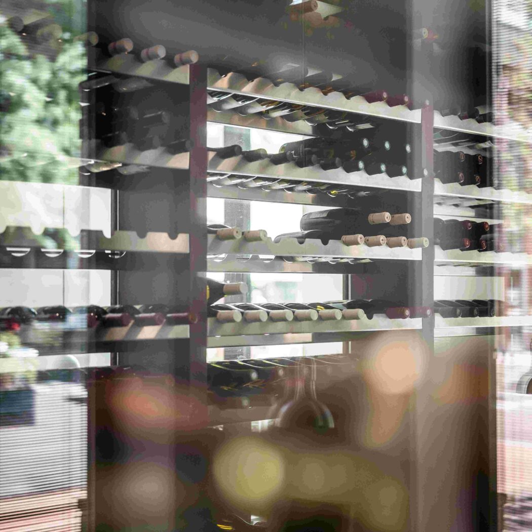 Wijnrek met rijen flessen, zichtbaar door reflecterend glas met boomreflecties.