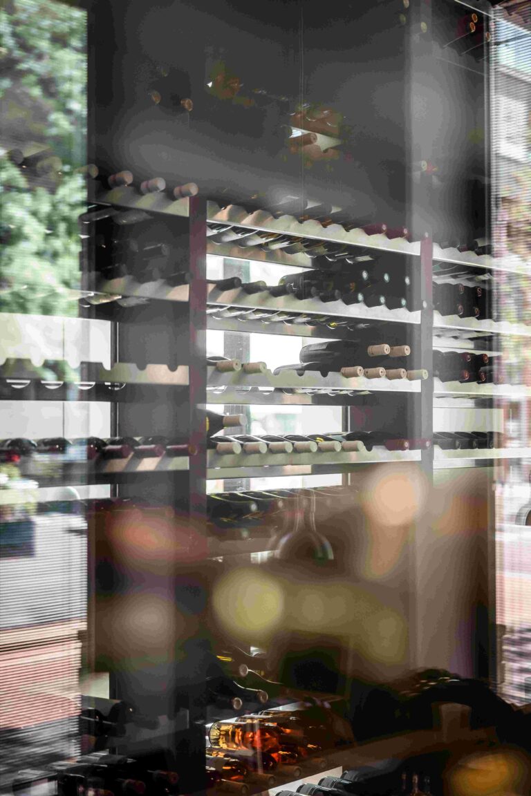 Wijnrek met rijen flessen, zichtbaar door reflecterend glas met boomreflecties.