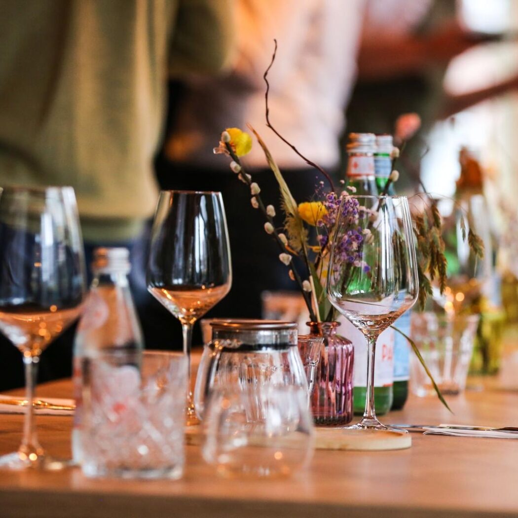 Gedekte houten tafel met wijnglazen, San Pellegrino flessen, bloemdecoraties en hapjes.