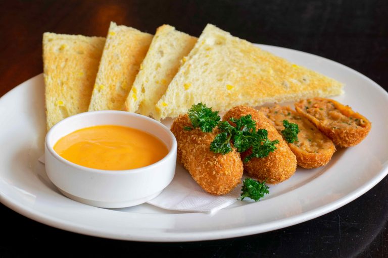 Wit bord met geroosterd brood, oranje dipsaus en knapperige gefrituurde snacks, gegarneerd met peterselie.