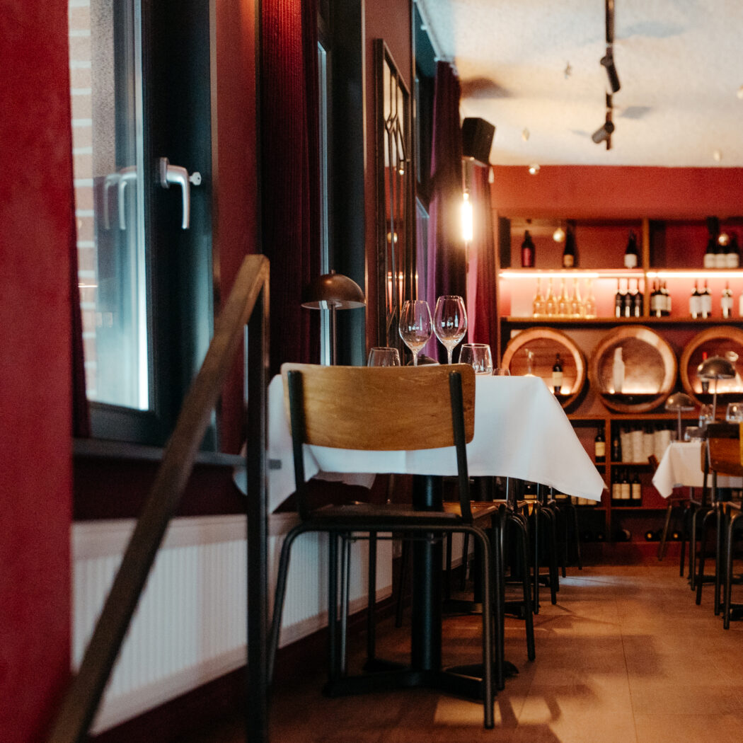 Sfeervol restaurant met rood-getinte muren, tafels met wijnglazen, en een wijnrek met houten vaten.