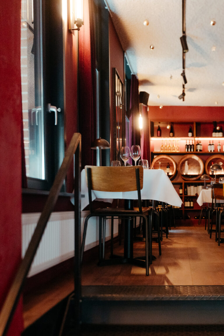Sfeervol restaurant met rood-getinte muren, tafels met wijnglazen, en een wijnrek met houten vaten.