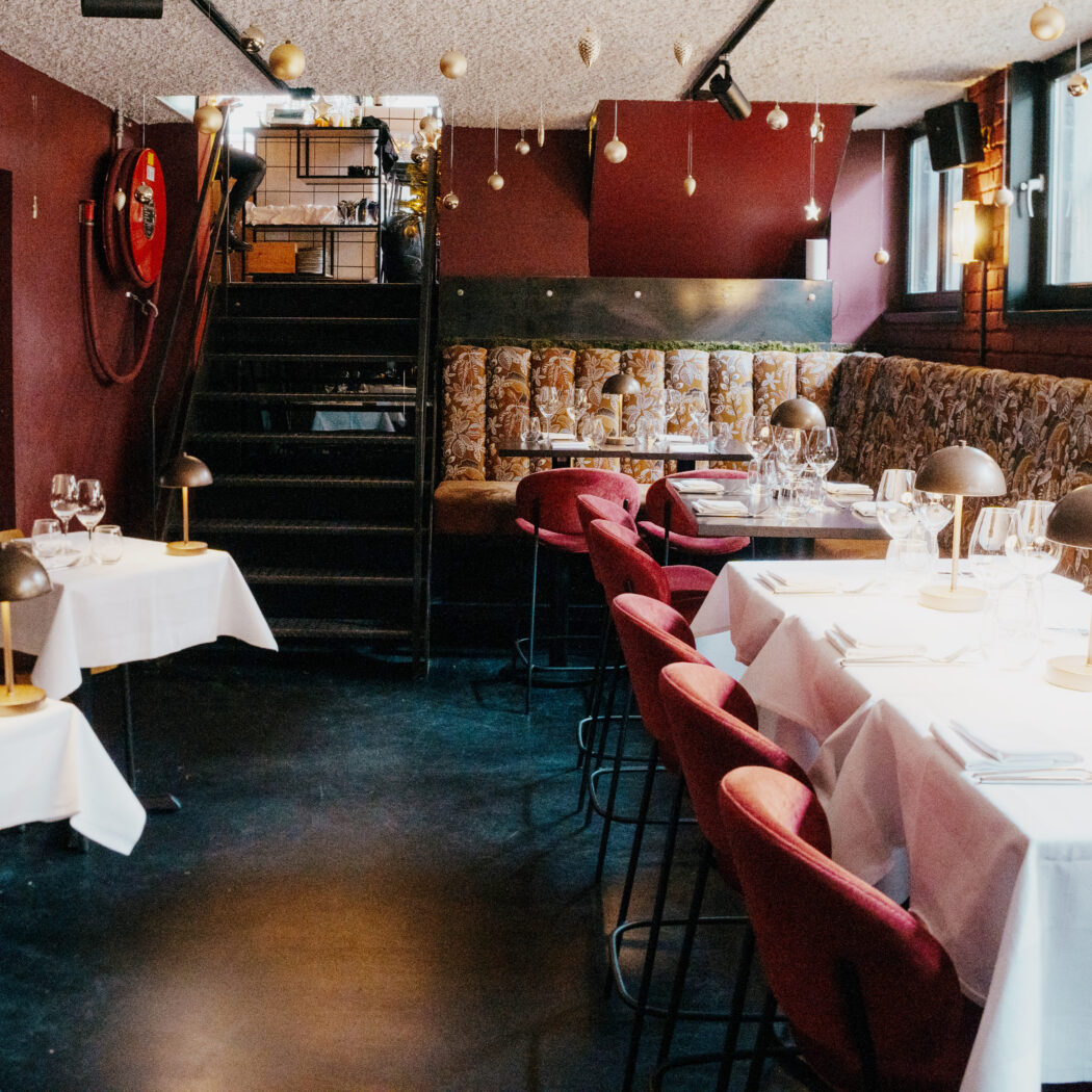 Sfeervol restaurantinterieur met rode muren, wit gedekte tafels, fluwelen stoelen en feestelijke plafonddecoraties.
