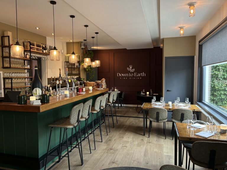 Gezellig restaurant interieur met een lange donkergroene bar, hoge barkrukken en gedekte tafels; Down to Earth FINE DINING op de muur.