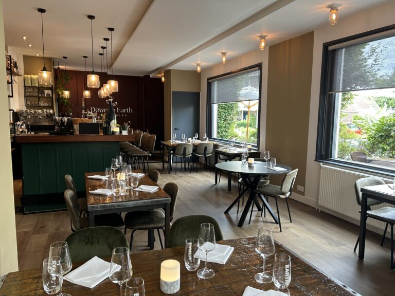 Sfeervol interieur van restaurant Down To Earth Dining met houten tafels, olijfgroene stoelen, een donkergroene bar en grote ramen.