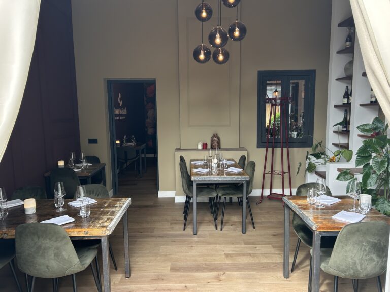Sfeervol restaurant met gedekte rustieke houten tafels, donkergroene fluwelen stoelen en verlichting. JUMBO TAH in doorloop.