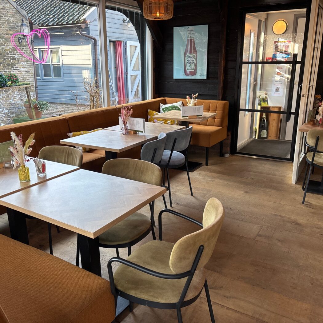 Sfeervol restaurant met lichte houten tafels, bruine banken, olijfgroene stoelen en een neon roze hart.