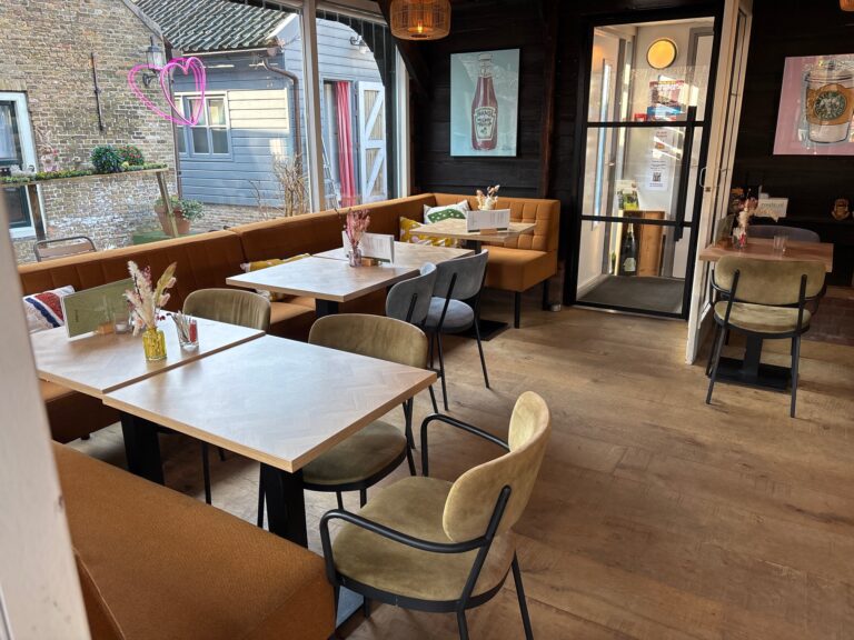 Sfeervol restaurant met lichte houten tafels, bruine banken, olijfgroene stoelen en een neon roze hart.