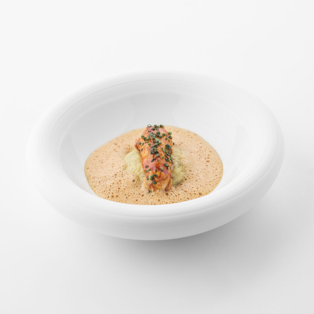 Gepresenteerd kreeftgerecht met schuimige bisque, bieslook en puree in een witte design kom.