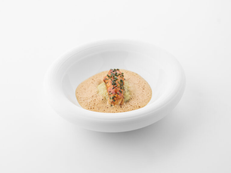 Gepresenteerd kreeftgerecht met schuimige bisque, bieslook en puree in een witte design kom.