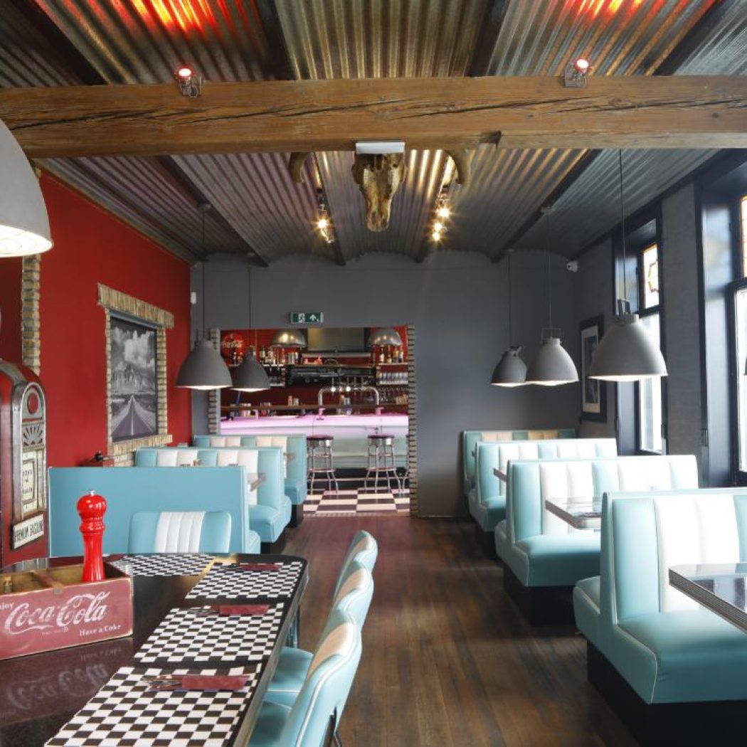 Sfeervol retro diner restaurant interieur met blauw-witte zithoeken, zwart-wit dambord tafels en een rode vintage benzinepomp.