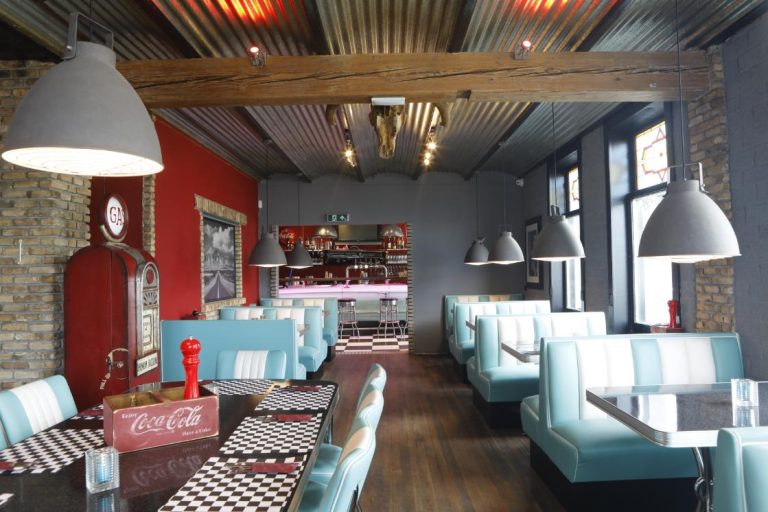 Sfeervol retro diner restaurant interieur met blauw-witte zithoeken, zwart-wit dambord tafels en een rode vintage benzinepomp.