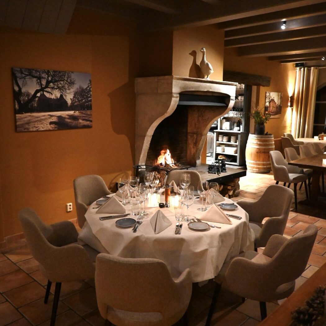 Ronde tafel met kaarsen en bestek in een sfeervol restaurant met brandende open haard.