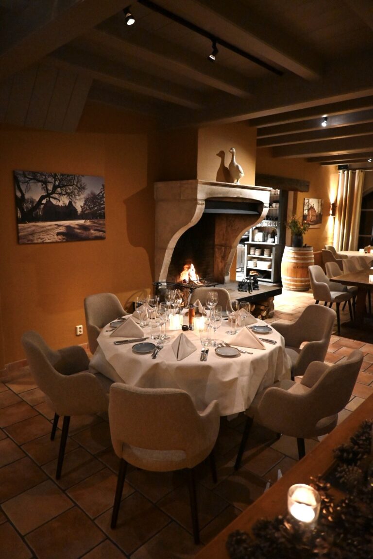 Ronde tafel met kaarsen en bestek in een sfeervol restaurant met brandende open haard.
