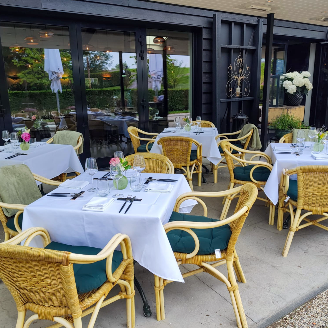 Restaurant terras met gedekte tafels, rotan stoelen met donkergroene kussens en bloemdecoraties.