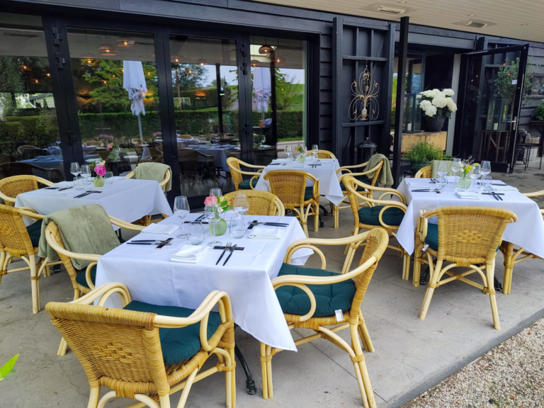 Restaurant terras met gedekte tafels, rotan stoelen met donkergroene kussens en bloemdecoraties.