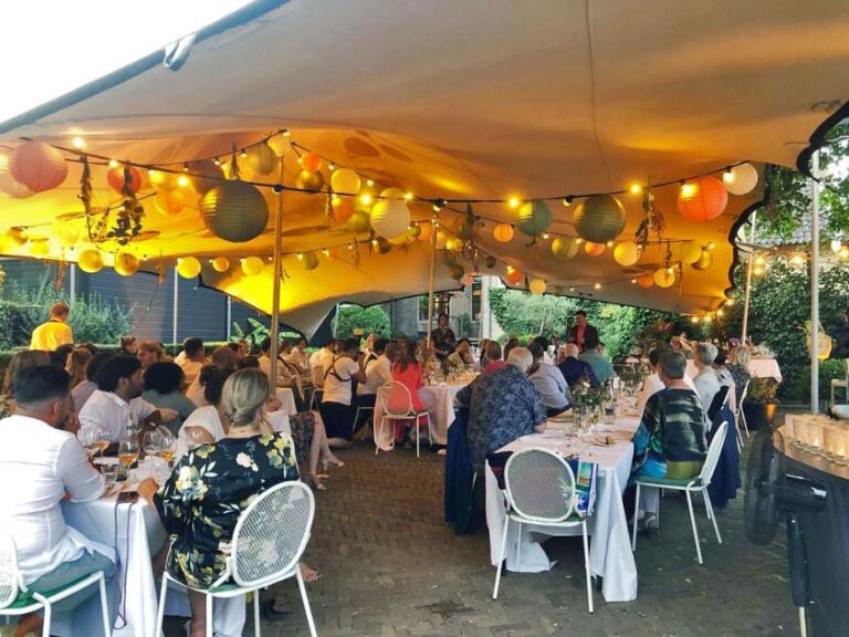 Gasten dineren buiten onder een tent versierd met kleurrijke lampionnen en sfeervolle lichtslingers.