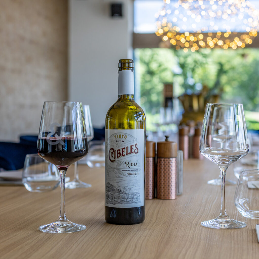 Fles Cibeles Rioja rode wijn en een glas rode wijn op een gedekte houten tafel.