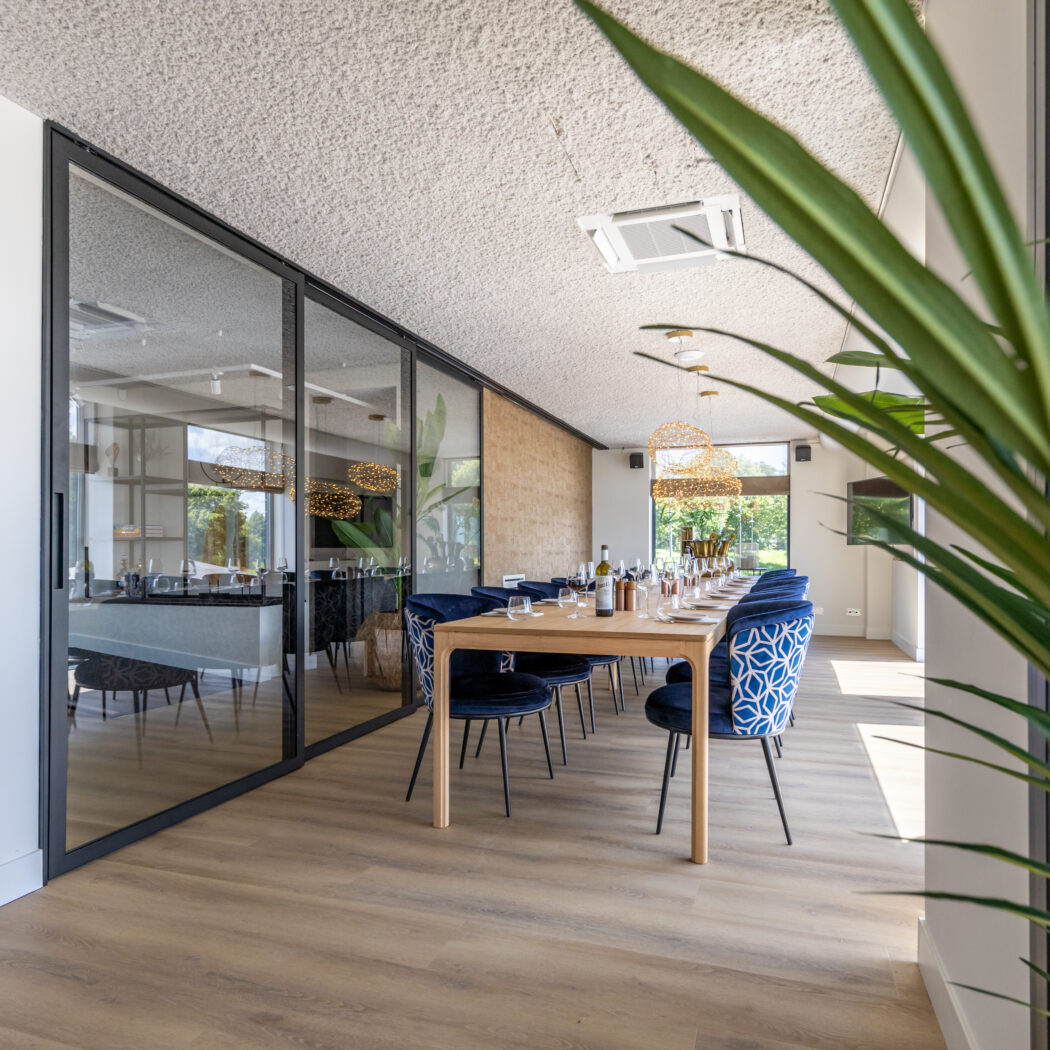 Lichte, moderne dinerruimte met lange houten tafel, blauwe fluwelen stoelen en unieke gevlochten lampen.