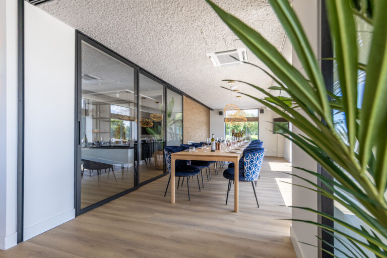 Lichte, moderne dinerruimte met lange houten tafel, blauwe fluwelen stoelen en unieke gevlochten lampen.