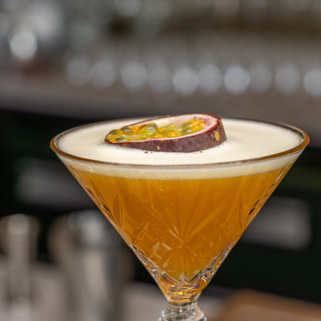 Oranje cocktail met witte schuimlaag en halve passievrucht in een geslepen martini glas.